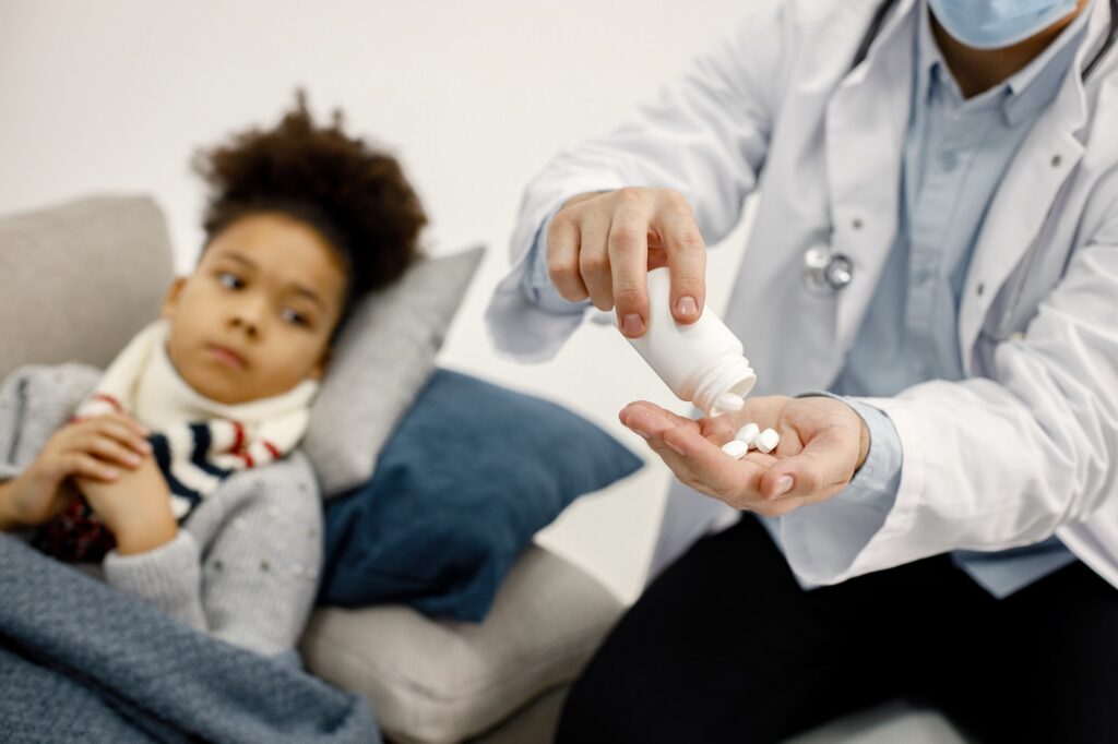 Cropped photo of male pediatrician give a medicines for sick little black girl